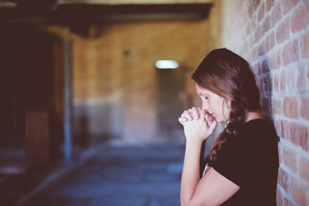 A young woman in a dark T-shirt stands in an alley as she meditates on God's Word to help fight anxiety.