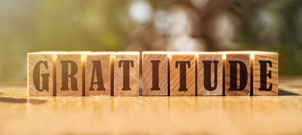 Wooden blocks with the word "gratitude" sit on a wooden table to encourage gratitude in our hearts.