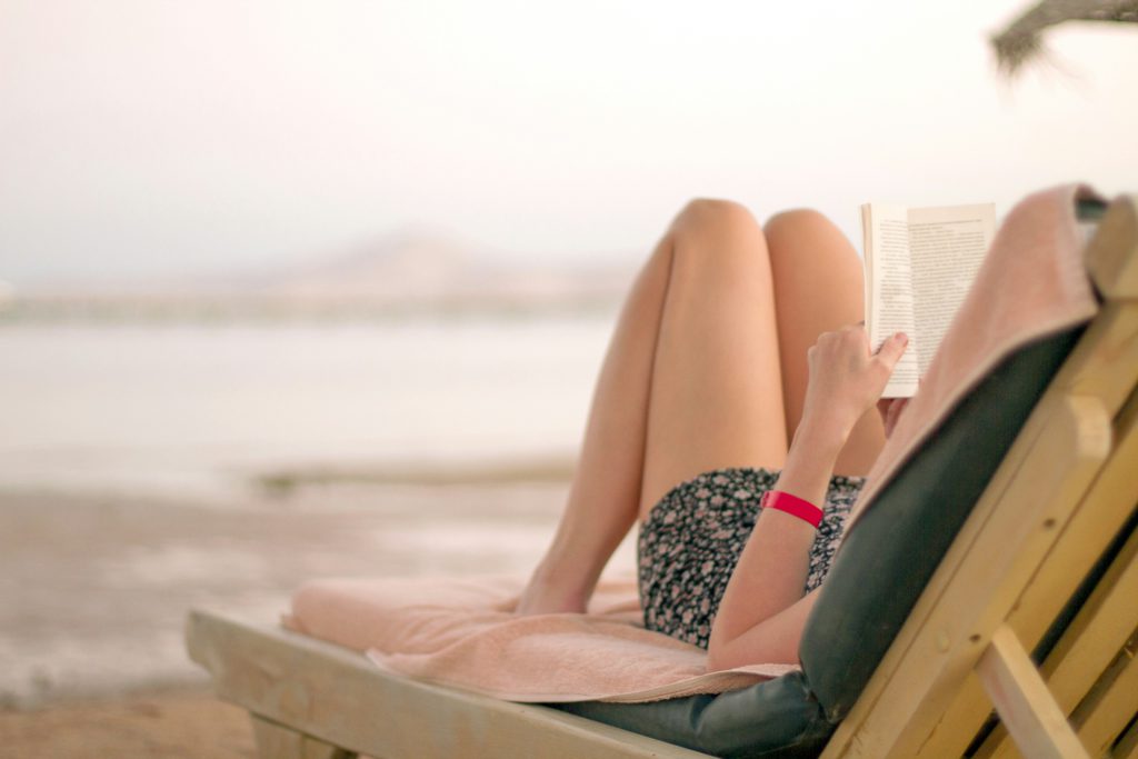 A woman reads a book in a chair on the beach, learning to find rest.