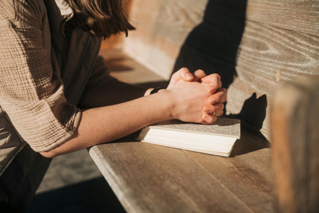a young woman kneels by a wooden pew with folded hands on a Bible as she prays powerful life prayers